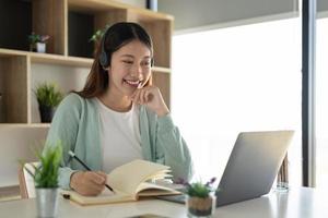 Concéntrese en un trabajador autónomo gial asiático que usa auriculares y se comunica con el cliente a través de una videollamada. tutora profesional milenaria y agradable que da clases de idiomas en línea. foto