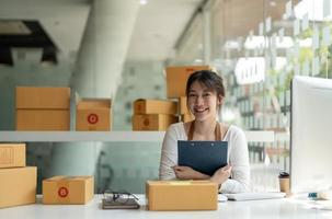Portrait young attractive asia female owner startup look at camera work happy with box at home prepare parcel delivery in sme supply chain, procurement, omnichannel ecommerce online concept photo
