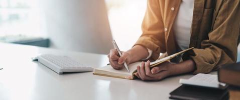 foto recortada de una mujer escribiendo haciendo una lista tomando notas en el bloc de notas trabajando o aprendiendo en una computadora portátil en el interior: curso educativo o capacitación, seminario, concepto de educación en línea