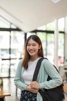 retrata a una joven estudiante asiática sosteniendo una tableta digital en la universidad parada frente a un casillero con mochila. foto
