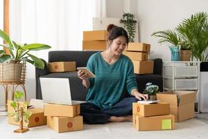 Asian woman entrepreneur using calculator with pencil in her hand, calculating financial expense at home office,online market packing box delivery,Startup successful small business owner, SME, concept photo