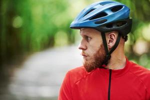 Looking to the side. Cyclist on a bike is on the asphalt road in the forest at sunny day photo