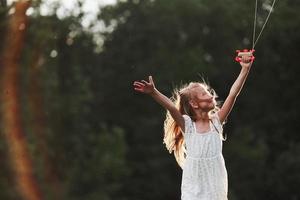 At countryside. Happy girl in white clothes have fun with kite in the field. Beautiful nature photo