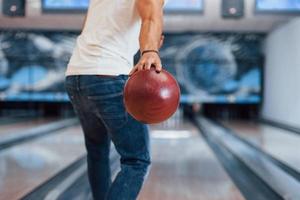 Weekend activities. Rear particle view of man in casual clothes playing bowling in the club photo