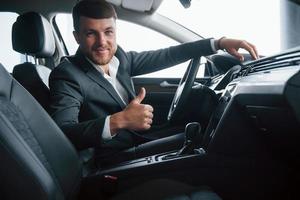 Eso es genial. hombre de negocios moderno probando su auto nuevo en el salón del automóvil foto