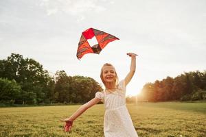 Running to the camera. Happy girl in white clothes have fun with kite in the field. Beautiful nature photo