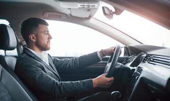 preciosa iluminación. hombre de negocios moderno probando su auto nuevo en el salón del automóvil foto