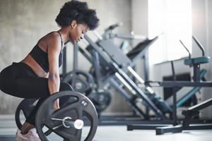Side view. African american woman with curly hair and in sportive clothes have fitness day in the gym photo