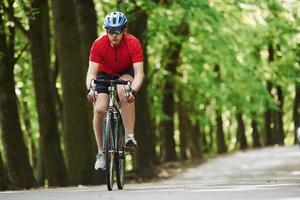 una sola persona ciclista en bicicleta está en la carretera asfaltada en el bosque en un día soleado foto