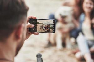 Using smartphone. Group of people have picnic on the beach. Friends have fun at weekend time photo