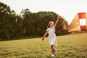 buen lugar. chica feliz vestida de blanco diviértete con cometa en el campo. Hermosa naturaleza foto