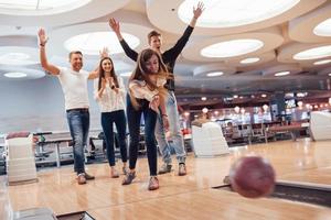 Supporting a girl. Young cheerful friends have fun in bowling club at their weekends photo