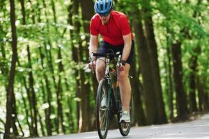 Spring time activities. Cyclist on a bike is on the asphalt road in the forest at sunny day photo