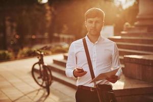 Looking at the camera. Businessman in formal clothes with black bicycle is in the city photo