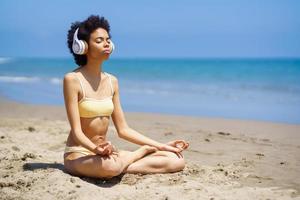 Tranquil black woman meditating in Lotus pose on sandy seacoast photo