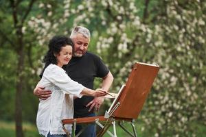 mira esto. pareja madura tiene días libres y trabaja en la pintura juntos en el parque foto