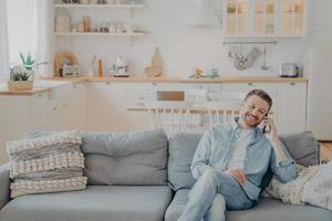 Young man talking on phone with his friend while sitting on couch photo