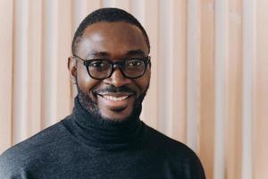 Elegant confident Afro american businessman in glasses posing while standing in modern office photo