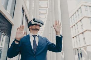 Young modern businessman in VR goggles on head working in augmented reality world and smiling photo