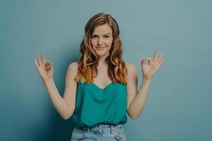 Confident joyful young woman in casual clothes gesturing ok sign with both hands in studio photo