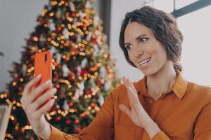 Happy hispanic woman talking by video call with family while enjoying winter holidays at home photo