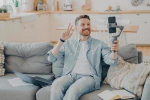 Positive young man showing peace sign during video call while sitting on couch photo