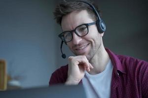 hombre alegre consultor de centro de llamadas de habla alemana en auriculares con micrófono trabaja de forma remota desde casa foto