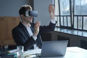 Male office worker in vr headset interacting with digital interface while sitting at desk photo
