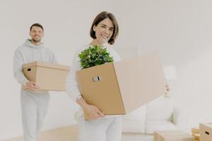 Happy young couple enter own modern house, buy real estate, carry cardboard boxes with indoor plant and other personal stuff, buy new house for living, have moving day. People and property concept photo