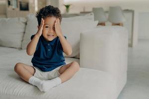 Cute little boy with curly hair enjoying game of hide and seek at home photo