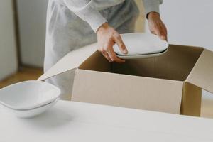 Cropped image of unknown faceless busy man unpacks boxes with dishes, holds white plates, moves in new apartment, tidies up at kitchen, has moving day. Bring out new plates. Relocation concept photo