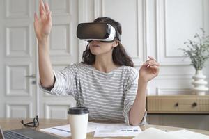 Concentrated woman bank accountant in VR headset sitting at desk at home office photo