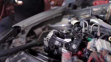 Car engine repair. The master attaches a part to the car engine with the help of light. video