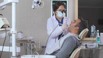 Dentist cleans patient's teeth. Dentist checks and cleans his patient's teeth video