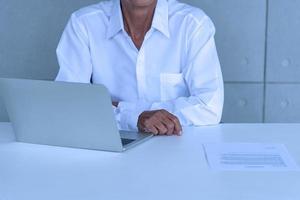 Work from home and social distancing concept. Asian business old man  working and drinking coffee at co-working space. Aging man using laptop meeting online. photo