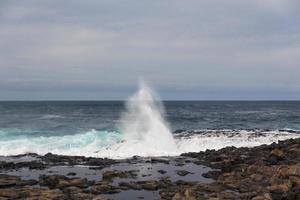 Turbulent ocean waves with white foam beat coastal stones photo