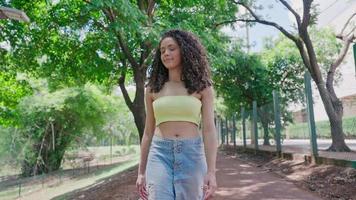 aantrekkelijke Latijns-vrouw wandelen in het park op een zonnige dag en glimlachen. het gezicht van een gelukkige mooie vrouw in de zomer buiten. slow motion 4k video