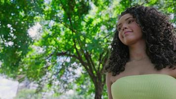 atractiva mujer latina caminando en el parque en un día soleado y sonriendo. el rostro de una hermosa mujer feliz en verano al aire libre. cámara lenta 4k video