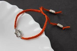 Orange handmade braded bracelet with chakra svadhishthana on the edge of a snow-white plate photo