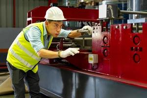 Asian industrial engineer worker is checking the setup value of metal sheet roll forming machine inside roof factory for safety industry construction concept photo