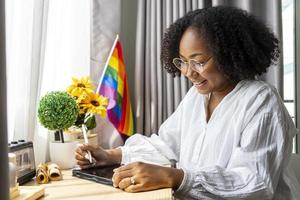 niña africana está trabajando en casa con la bandera del arco iris lgbtq en su mesa por salir del armario y la celebración del mes del orgullo para promover la diversidad sexual y la igualdad en la orientación homosexual foto