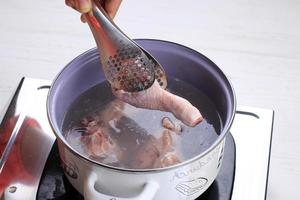 Indonesian Home Cooking Process, Female Hand Add Chicken Thigh Drumstick to the Pan using Tongs, Making Indonesian or Thai Style Curry, Traditional Asian Gourmet Called Opor Ayam photo