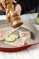 Woman Hand Grinding Pepper onto Fillet Fish on a Pan using Wooden Pepper Mill photo