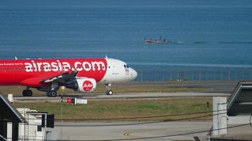 phuket, thailand 28 november 2017 - airasia airbus a320 hs aby taxiënd voor vertrek vanaf de luchthaven van phuket, en longtail vissersboot op de achtergrond video