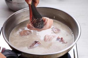 Indonesian Home Cooking Process, Female Hand Add Chicken Thigh Drumstick to the Pan using Tongs, Making Indonesian or Thai Style Curry, Traditional Asian Gourmet Called Opor Ayam photo