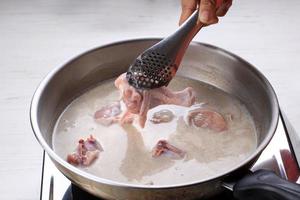 Indonesian Home Cooking Process, Female Hand Add Chicken Thigh Drumstick to the Pan using Tongs, Making Indonesian or Thai Style Curry, Traditional Asian Gourmet Called Opor Ayam photo