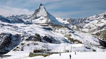 Train passing by the Matterhorn mountain in Zermatt. Railroad vehicle running towards Gornergrat station. Snow covered landscape against blue sky in Alps during winter. video