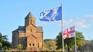 vue statique drapeaux de l'ue et géorgiens sur la place de l'europe avec panorama de l'église dans la capitale tbilissi. intégration de la géorgie au concept de l'ue video