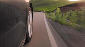 Side view wheel spin in fast motion on standard grey asphalt surface uphill in green mountains top video