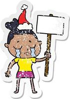 distressed sticker cartoon of a crying woman with protest sign wearing santa hat vector
